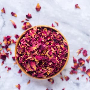 May include: A wooden bowl filled with dried rose petals. The petals are a mix of pink and red.
