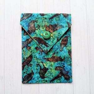 May include: A blue fabric envelope with a green button closure. The fabric features a repeating pattern of black birds on a blue and green background.