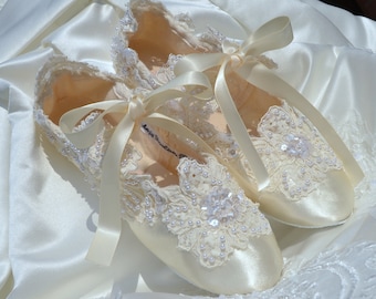 May include: A pair of ivory satin ballet-style flats featuring intricate white lace overlays, delicate pearl bead embellishments, and clear sequins. The shoes are secured with matching ivory satin ribbon ties that are tied in bows at the top.