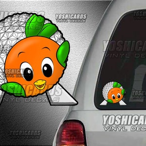 May include: A vinyl decal featuring a cartoon orange bird with green feathers, holding a white geodesic dome. The decal is on a car window with the text "YOSHICARDS VINYL DECALS" printed on the window.