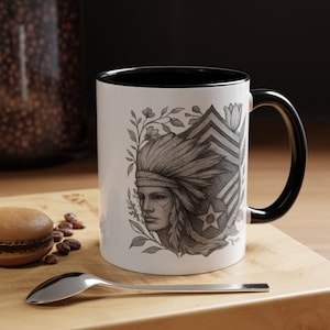 May include: White ceramic mug with a black interior and handle. The mug features a detailed pencil-style drawing of a Native American person with a headdress, surrounded by floral elements and a star.