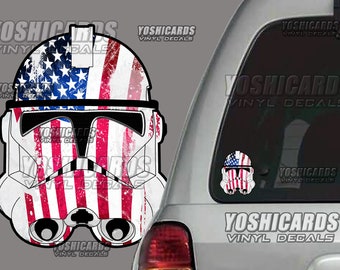 May include: A white vinyl decal of a Stormtrooper helmet with a distressed American flag design. The helmet features red and white stripes and a blue field of stars. The decal is shown on a car window. The text "YOSHICARDS VINYL DECALS" is visible.