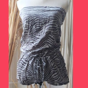 May include: A strapless, zebra-print top and shorts set. The top is gathered at the waist and the shorts have a drawstring. The fabric has a black and white pattern. The outfit is displayed on a mannequin.
