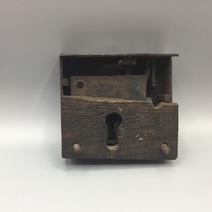 May include: A vintage wooden door lock with a metal latch and keyhole. The lock is in a disassembled state, showing the internal workings.