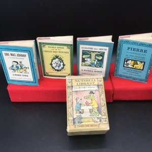 May include: A collection of miniature children's books, including titles like "One Was Johnny" and "Chicken Soup with Rice." The books have colorful covers and illustrations, with titles and author names visible. The books are displayed on a red surface.