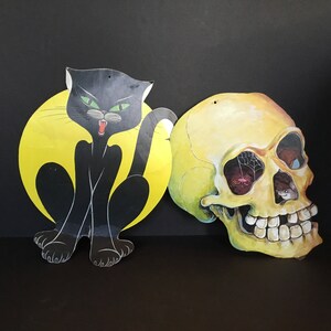 May include: A black cat with green eyes and a yellow moon behind it, and a yellow skull with a spider web over one eye.