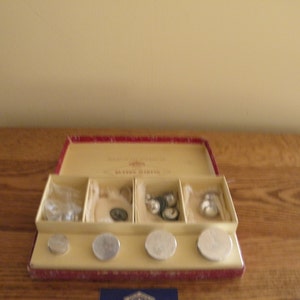 May include: A red box with a white label that says "Button Tack Co. Button Tacks" and contains a variety of buttons and button tacks.