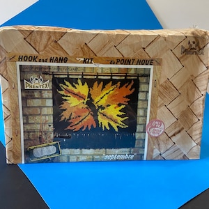 May include: A vintage latch hook kit for a wall hanging featuring a design of autumn leaves in shades of orange, yellow, and brown. The kit is labelled "Hook and Hang Kit du Point Noue" and "septembre" with the brand name "Phentex".