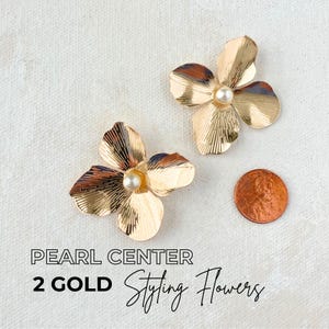May include: Two gold-coloured flower-shaped styling accessories with pearl centres. The accessories are next to a penny for size comparison. The text on the image reads "Pearl Center 2 Gold Styling Flowers."