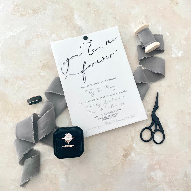 May include: A white wedding invitation with black calligraphy that reads "you & me forever". The invitation includes the names "Try & Mury" and details for their wedding ceremony on August 13, 2023, at Maumee Bay State Park in Oregon, Ohio.