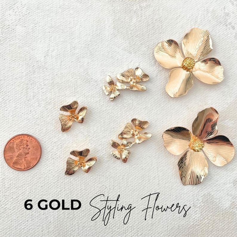May include: Six gold-coloured styling flowers in various sizes are arranged on a white surface. The flowers have a detailed petal design and a textured finish. A penny is included for size reference. The text "6 GOLD Styling Flowers" is at the bottom.