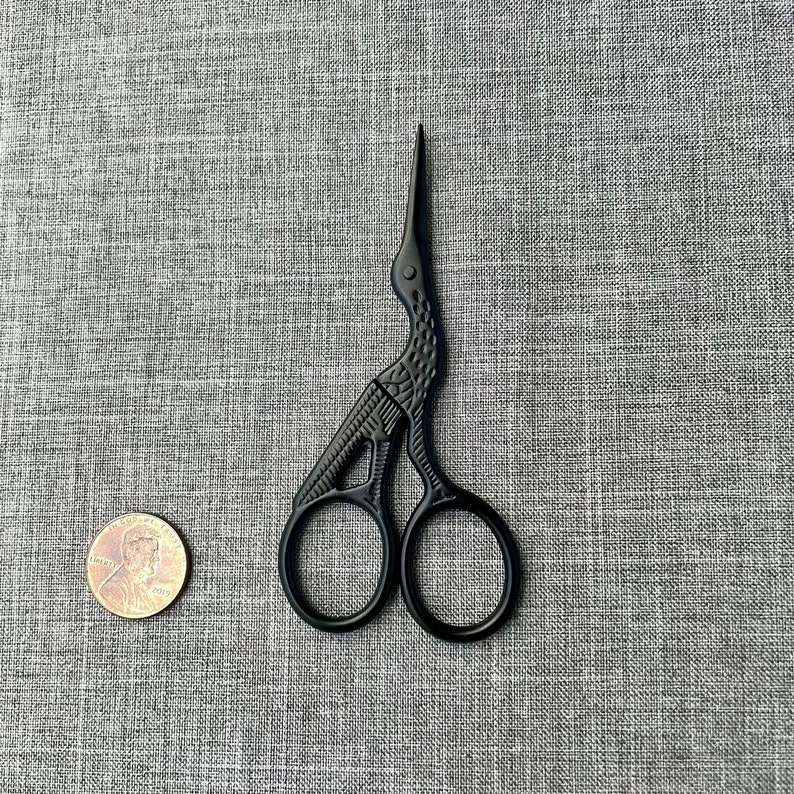 May include: Black metal scissors with a bird design. The scissors are closed and have a small, round handle.