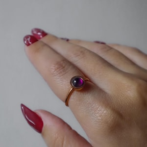 May include: A gold ring with a purple gemstone. The ring is on a person's finger.