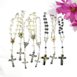 May include: A set of six pearl and black bead rosaries with silver and gold crosses. Each rosary features a different religious image.