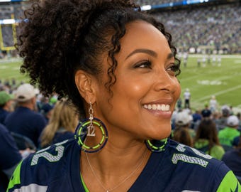 May include: A pair of hoop earrings featuring concentric circles of dark blue and neon green beads. A silver-toned charm shaped like the number 12 hangs from the centre of each earring. The earrings are worn with a dark blue and neon green jersey.