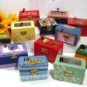 Puede incluir: Una colección de doce cajas de madera decorativas, cada una con diseños y colores únicos. Las cajas presentan varios adornos, incluidos patrones florales, joyas y cierres ornamentados. Las cajas son de varios colores, como rojo, azul, verde y amarillo.