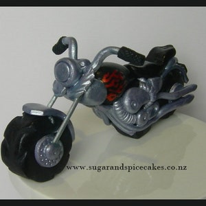 May include: A silver and black motorcycle cake topper with red and orange flames on the side. The motorcycle has a black seat and a black exhaust pipe.