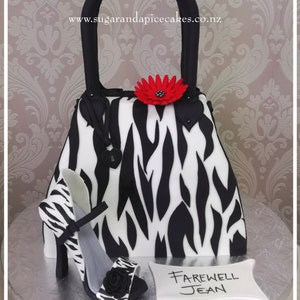May include: A black and white zebra print handbag cake with a red flower and a matching zebra print high heel shoe. The cake is decorated with the words "Farewell Jean".