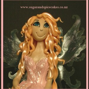 May include: A pink fairy cake topper with a smiling face, long blonde hair, and silver wings. The fairy is wearing a pink dress with a ruffled neckline.