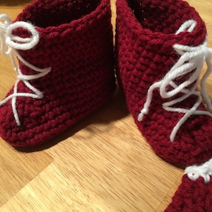 Puede incluir: Un par de botines de beb&eacute; hechos a mano, tejidos a ganchillo, de color rojo intenso. Los botines tienen cordones blancos y un patr&oacute;n de puntada texturizada. Los botines est&aacute;n dise&ntilde;ados para parecer botas en miniatura.