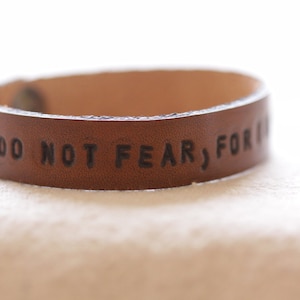 Peut inclure: Un bracelet en cuir marron avec le texte "DO NOT FEAR, FOR I AM WITH YOU" gravé dessus.