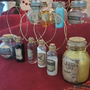 May include: A collection of eight glass bottles with cork tops and labels, decorated with gold wire, hanging from a Christmas tree. The labels include names like "Floo Powder", "Bezoars", "Liquid Luck", and "Truth Potion".