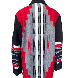 May include: A wool coat with a geometric pattern in red, gray, black, and white. The coat features a black collar and sleeves with red and white accents. The back of the coat showcases a striking diamond-shaped design.
