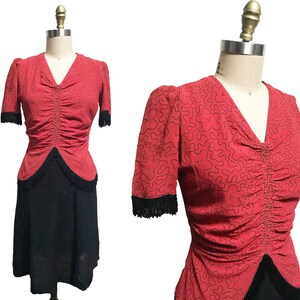 Pode incluir: Um vestido vermelho com saia preta e top vermelho com padr&atilde;o preto e branco. O top tem um corpete franzido e um decote em V. A saia &eacute; em A e tem uma bainha de franjas pretas.