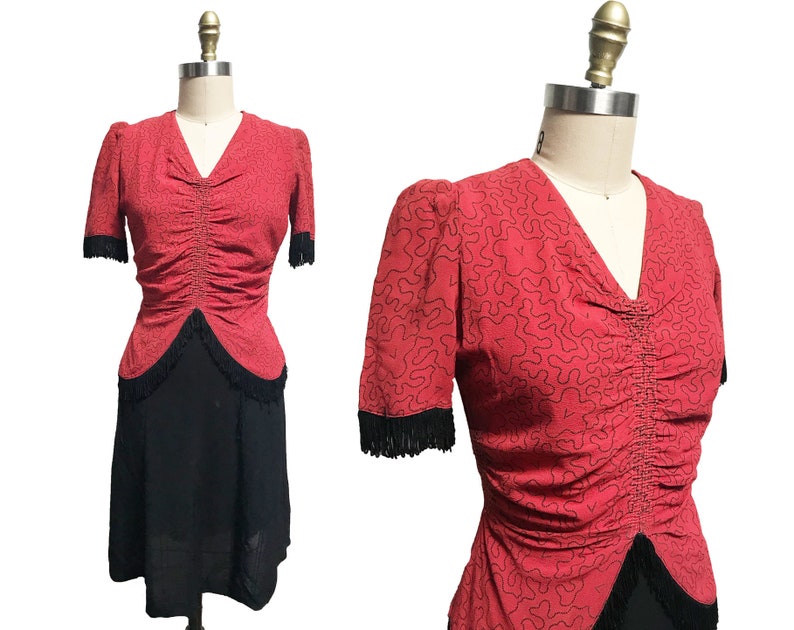 Pode incluir: Um vestido vermelho com saia preta e top vermelho com padr&atilde;o preto e branco. O top tem um corpete franzido e um decote em V. A saia &eacute; em A e tem uma bainha de franjas pretas.