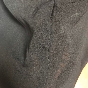 Pode incluir: Close-up de um tecido preto com uma costura que percorre o centro. O tecido tem uma superf&iacute;cie ligeiramente texturizada.