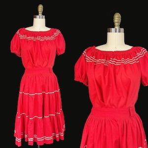 May include: A vintage red dress with a tiered skirt and short, puffed sleeves. The dress features white embroidered trim along the neckline and skirt tiers. The dress is displayed on a mannequin against a black background.