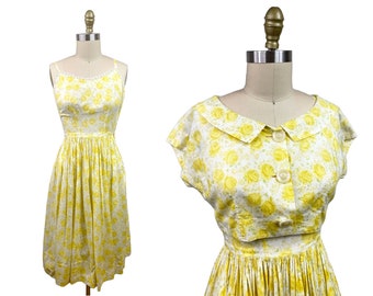 May include: A yellow and white floral print dress with a matching cropped top. The dress has a fitted bodice and a full skirt. The top has a Peter Pan collar and short sleeves.