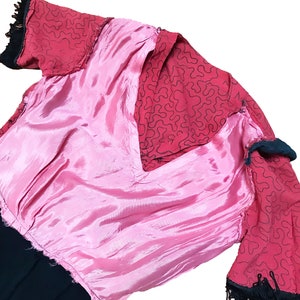 Pode incluir: Um vestido rosa e vermelho com uma borda preta. O vestido tem um decote em V e mangas curtas. O tecido &eacute; de material sedoso.