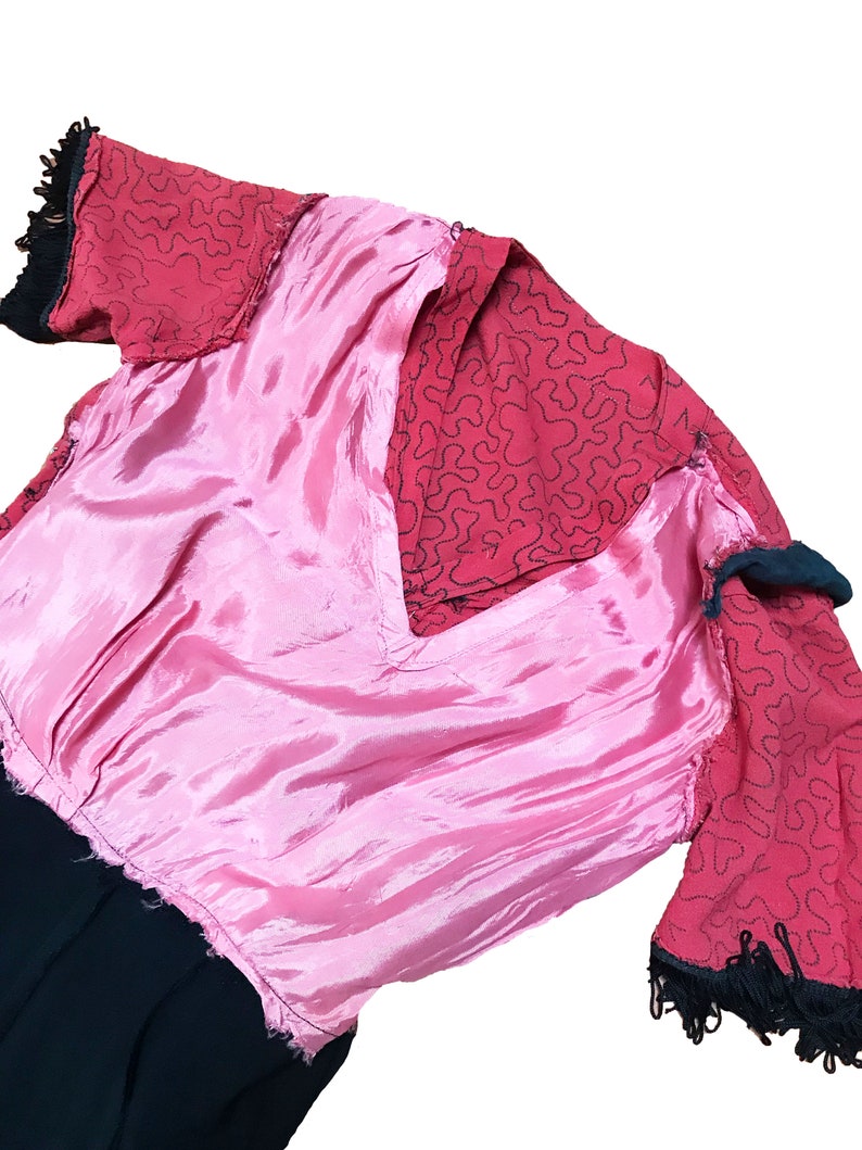 Pode incluir: Um vestido rosa e vermelho com uma borda preta. O vestido tem um decote em V e mangas curtas. O tecido &eacute; de material sedoso.