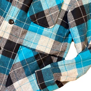May include: A blue, black, and white plaid flannel shirt with a button-up front and two pockets.