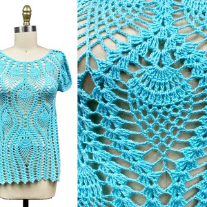 May include: A light blue crochet top with a delicate, lacy pattern. The top has a round neckline and short sleeves.