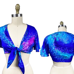 Könnte beinhalten: Ein blaues und pinkfarbenes Crop-Top mit Binde vorne. Das Oberteil hat kurze, gekräuselte Ärmel.