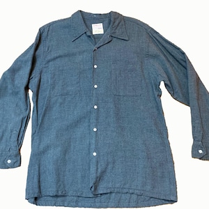 Może przedstawiać: Koszula z długim rękawem zapinana na guziki w stonowanym szaro-niebieskim odcieniu. Koszula posiada klasyczny kołnierzyk, dwie kieszenie na piersi i białe guziki. Tkanina wydaje się mieć strukturę. Mała metka jest widoczna w pobliżu kołnierza.