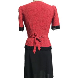 Pode incluir: Um vestido vermelho com uma borda de franjas pretas e uma saia preta. O vestido tem um decote em V e um la&ccedil;o na cintura.