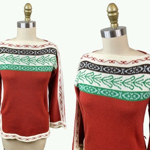 Puede incluir: Suéter de color óxido con cuello barco y mangas largas. La parte superior presenta una banda color crema con un patrón geométrico marrón y blanco, una banda verde con un diseño de hojas y una banda color crema con un patrón rojo.