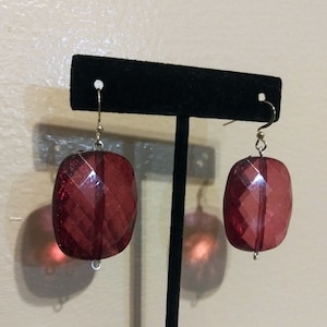 May include: A pair of red, faceted, rectangular dangle earrings with silver hooks.