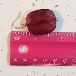 Pode incluir: Um par de brincos de vidro vermelho com um gancho de prata. Os brincos medem aproximadamente 2,5 cm de comprimento.