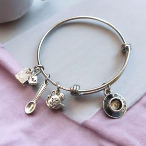 May include: Silver charm bracelet with tea-themed charms, including a tea bag, teapot, spoon, and teacup.
