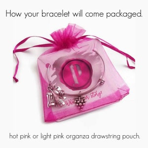 May include: A silver bracelet with a charm of a wine bottle and grapes comes packaged in a hot pink or light pink organza drawstring pouch. The pouch has a pink label with the text "What's your story?"