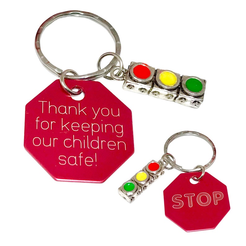 May include: Two red octagonal keychains with silver rings. One keychain says "Thank you for keeping our children safe!" and has a silver traffic light charm with red, yellow, and green lights. The other keychain says "STOP" and has a silver traffic light charm with red, yellow, and green lights.
