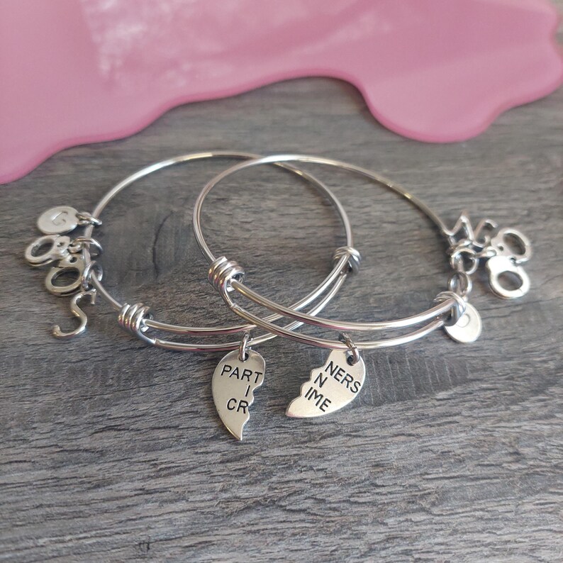May include: Two silver bangle bracelets with charms. One charm is a heart that says "Part in Crime" and the other charm is a heart that says "Ners in Time".