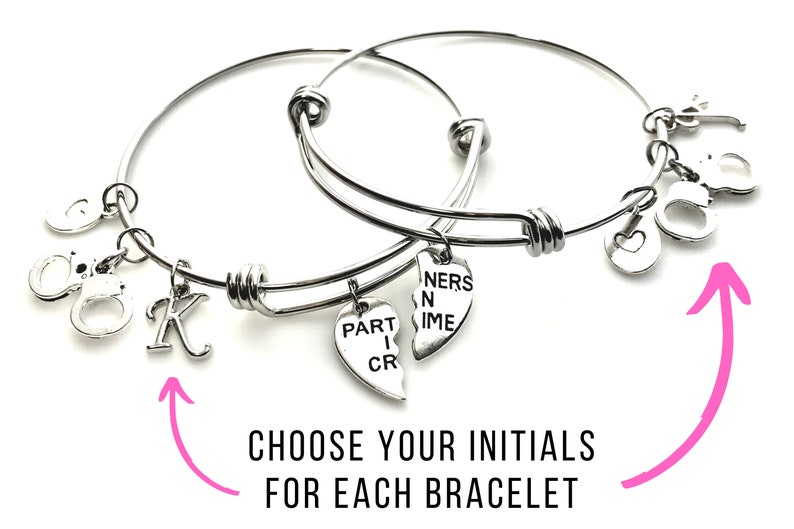 May include: Two silver bangle bracelets with charms. One charm says "Part in Crime" and the other says "Partners in Crime". The bracelets have a heart charm, a handcuff charm, and a letter charm. Choose your initials for each bracelet.