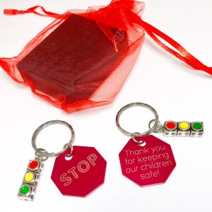May include: Two red stop sign keychain charms with a silver key ring and a traffic light charm. The charms say "STOP" and "Thank you for keeping our children safe!"