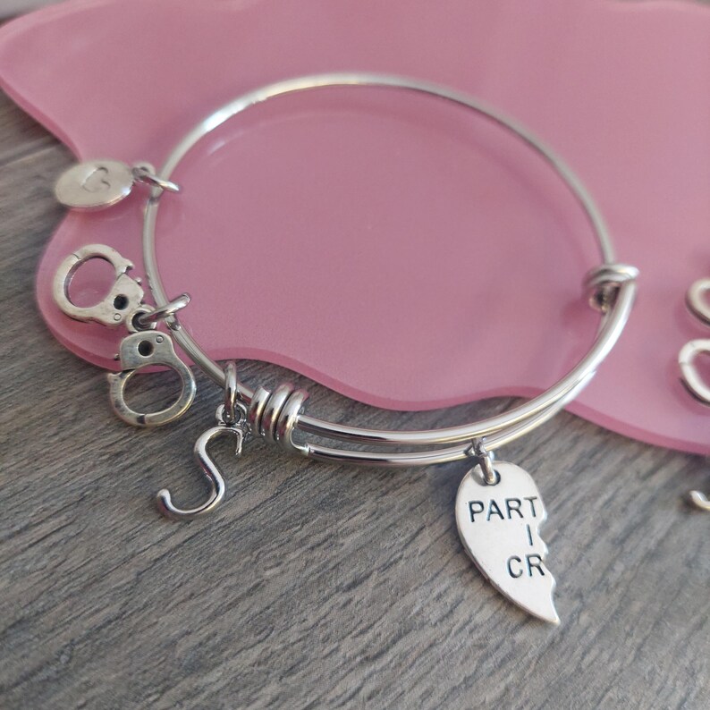 May include: A silver charm bracelet with a heart charm that says "Part 1 of 2" and other charms including handcuffs and a letter 'S'.