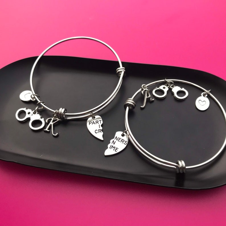 May include: Two silver charm bracelets with heart charms that say "Part in Crime" and "Ners in Time" and other charms including handcuffs and letters.